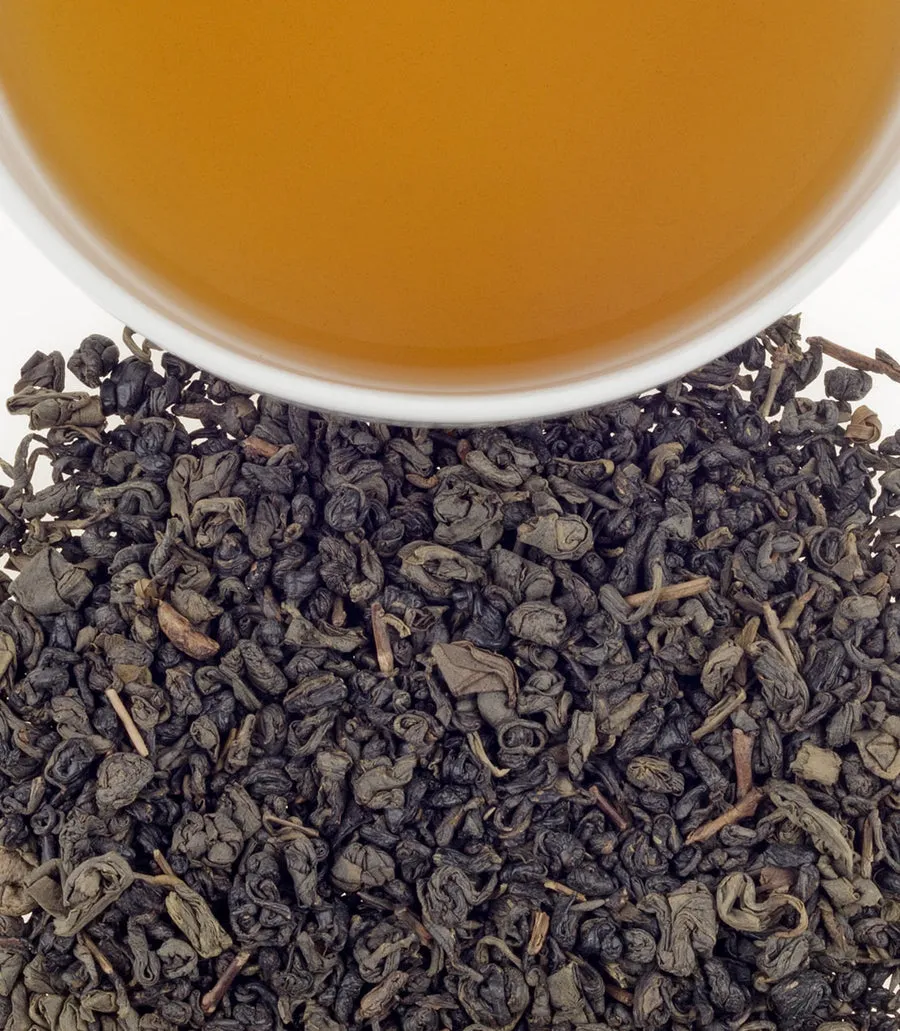Organic Gunpowder tea leaves with a cup of brewed tea above, showcasing rich color and texture.
