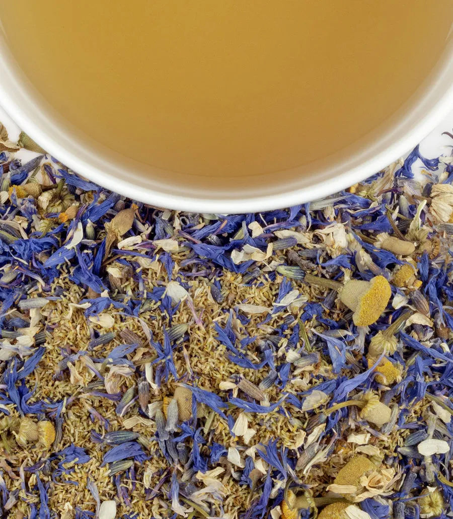 Yellow and blue herbal tea sachets in a tin, with dried flowers and brewed tea in a cup.