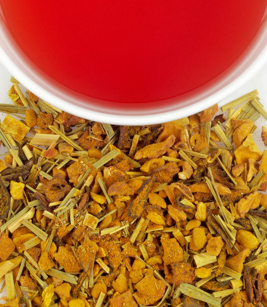 Organic ginger turmeric blend with dried herbs and a cup of vibrant red tea in the background.